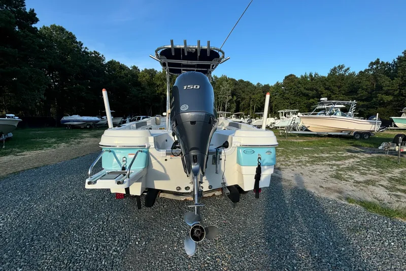Slide: The Image of 2018 NauticStar 211 Coastal boat with 150 HP engine, parked on gravel near trees. - 2
