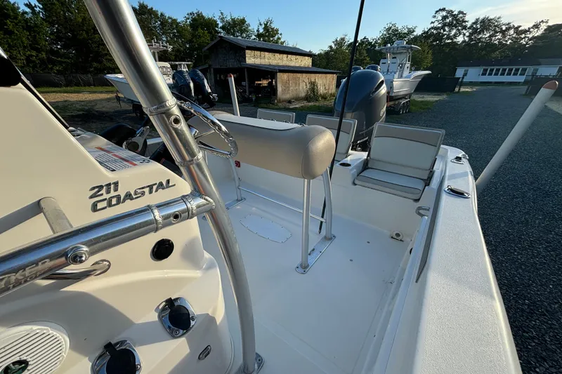 Slide: The Image of 2018 NauticStar 211 Coastal boat interior with seating and controls, parked outdoors. - 8