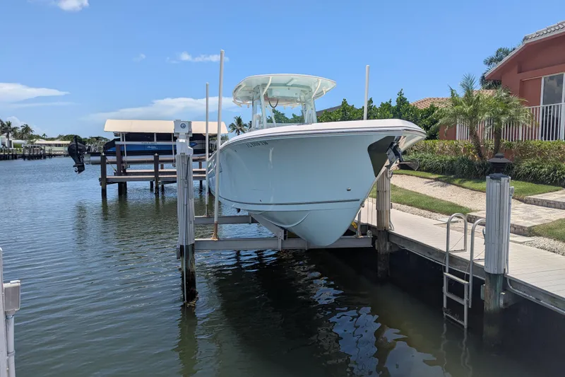 Slide: The Image of 2023 Sailfish 290 CC boat docked on a lift by waterfront property. - 2
