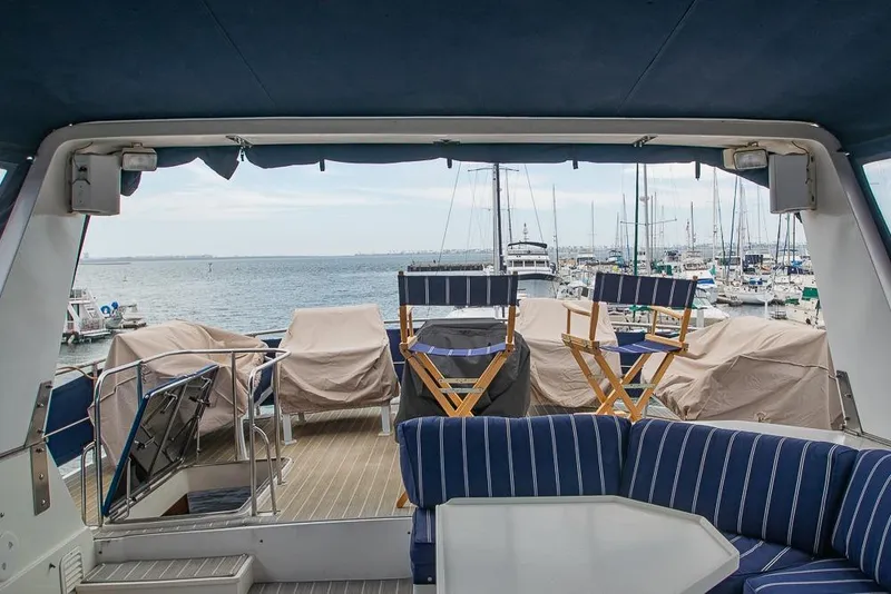 Slide: The Image of 1990 Kha Shing Flush Deck Motor Yacht with marina view, featuring striped seating and covered chairs. - 49