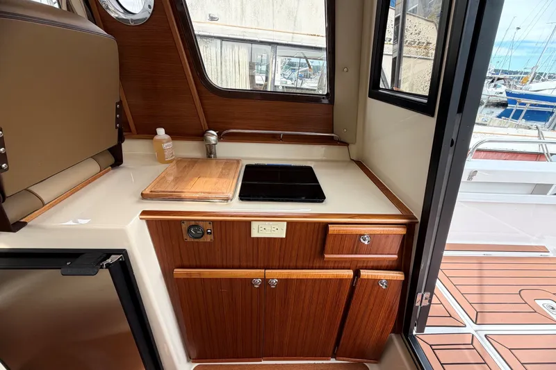 Slide: The Image of 2023 Ranger Tugs R-25 galley with wooden cabinetry, stove, and cutting board, overlooking marina. - 16