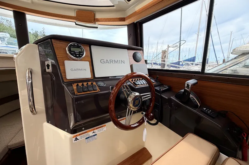 Slide: The Image of 2023 Ranger Tugs R-25 helm with Garmin navigation, wooden accents, and marina view. - 11
