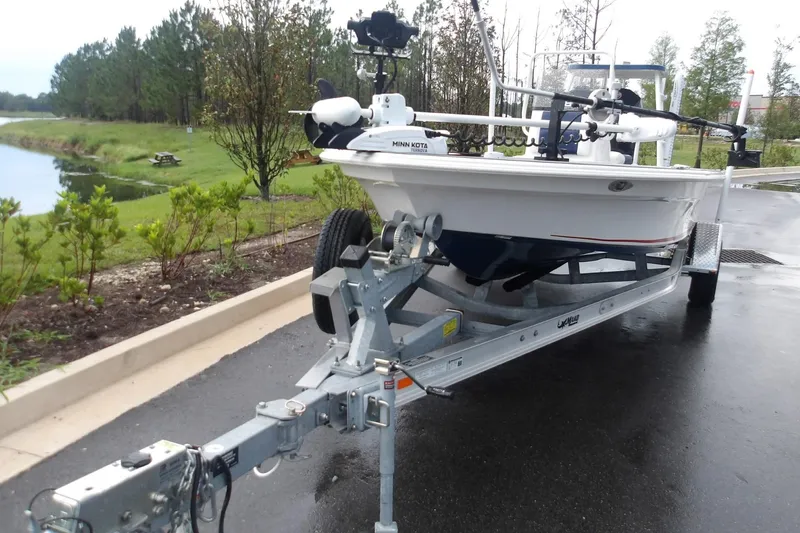 Slide: The Image of 2025 Mako 18 Pro Skiff Patriot Edition on trailer near a scenic waterway. - 2