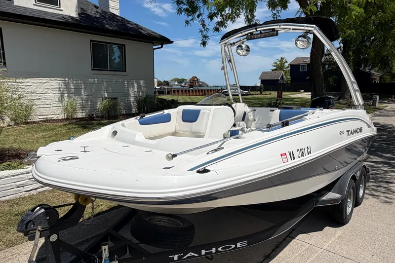 Slide: The Image of 2019 Tahoe 1950 boat on trailer, parked near a house with lush greenery. - 2
