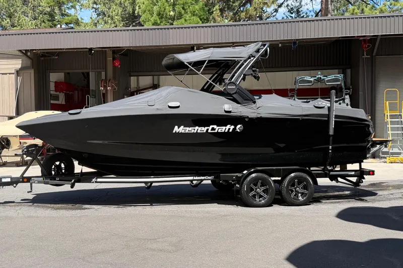 The Image of 2024 MasterCraft X24 boat on trailer, covered and parked outdoors. - 0