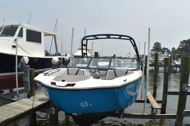 Slide: The Image of 2023 Yamaha Boats AR250 in marina, blue hull, sleek design, docked among other boats. - 2
