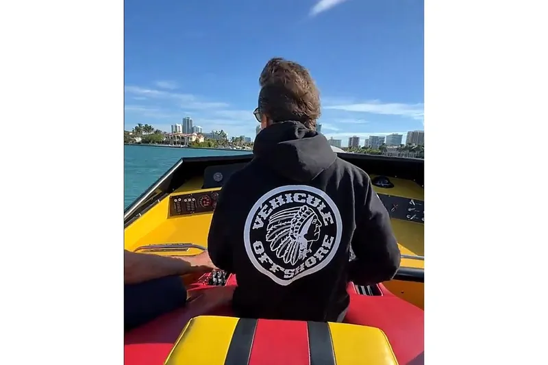 Slide: The Image of Person on Apache 47 boat, wearing "Vehicle Offshore" hoodie, enjoying sunny waterfront view. - 7