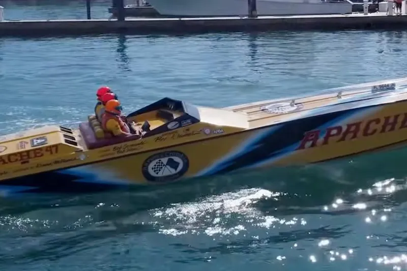Slide: The Image of 1987 Apache 47 speedboat cruising on water with two passengers wearing helmets. - 4