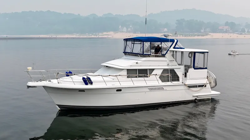 Slide: The Image of A white 1997 Carver 445 Aft Cabin Motor Yacht floats calmly on the water. It features a blue canopy and is set in a serene environment with wooded hills in the background. - 15