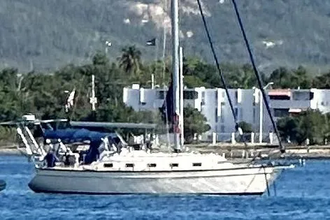 Slide: The Image of 2004 Island Packet 370 sailboat anchored near a coastal area with buildings and greenery. - 38