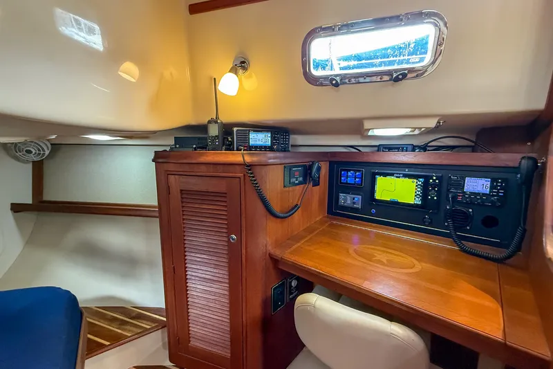 Slide: The Image of Navigation station inside 2004 Island Packet 370 sailboat, featuring wooden cabinetry and electronic equipment. - 21