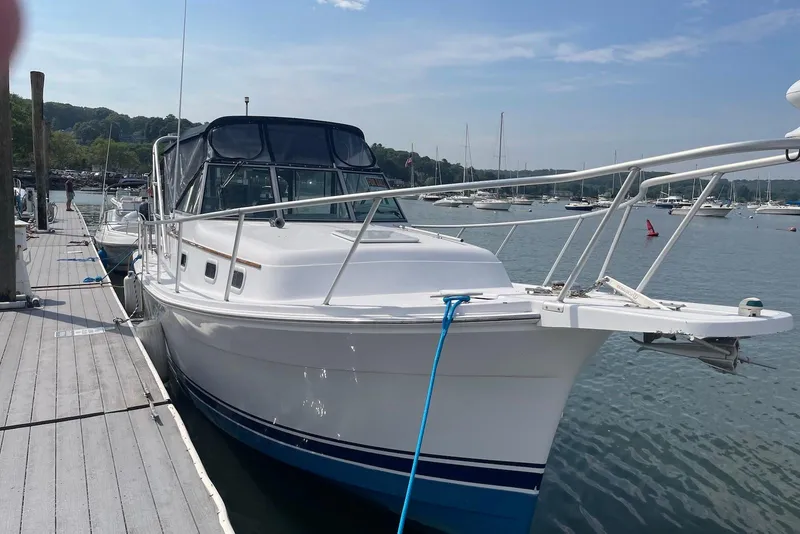 The Image of 1999 Mainship Pilot 30 docked at a marina, surrounded by calm waters and other boats. - 0