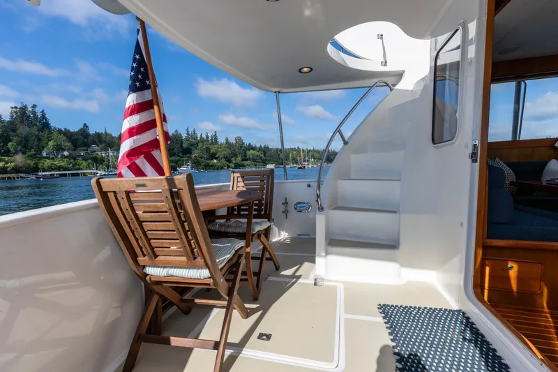 Slide: The Image of Outdoor seating on 2006 North Pacific 52 yacht with American flag, wooden chairs, and scenic water view. - 27