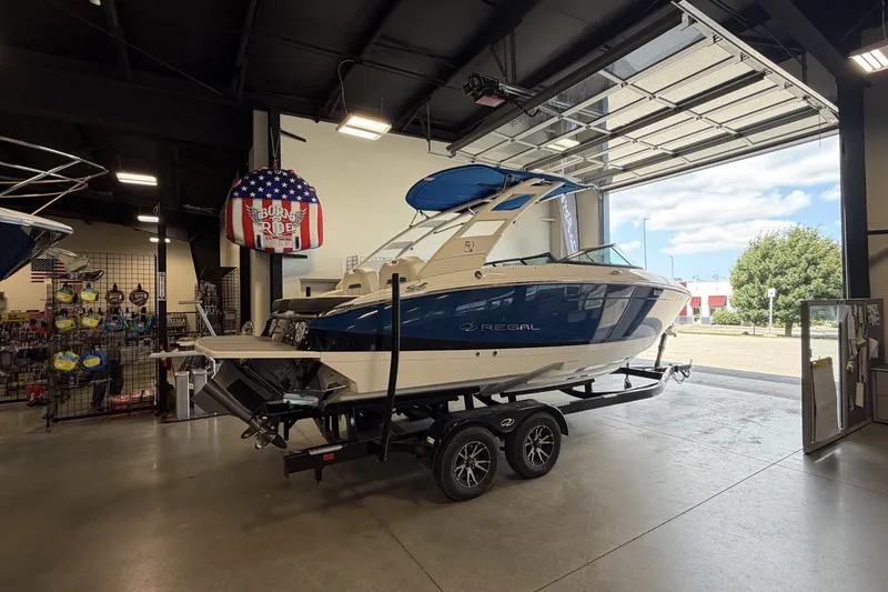 Slide: The Image of 2021 Regal LS4 Surf boat on trailer in showroom, featuring sleek blue and white design. - 1