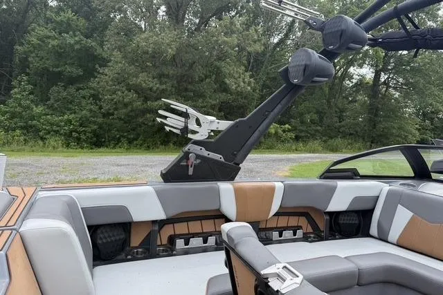 Slide: The Image of 2022 Malibu Wakesetter 23 MXZ interior with seating and wakeboard rack, surrounded by trees. - 17