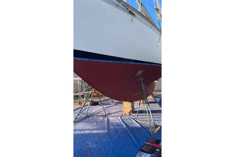 Slide: The Image of Alajuela 38 MKI 1977 sailboat on stands, hull painted red, under clear blue sky. - 66