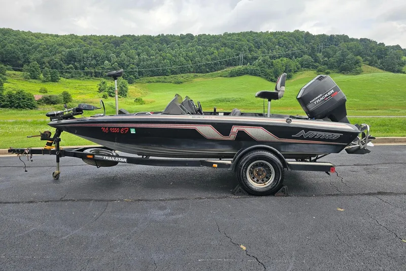 The Image of 1994 Nitro 180 FS boat on trailer, parked on asphalt with lush green hills in background. - 1
