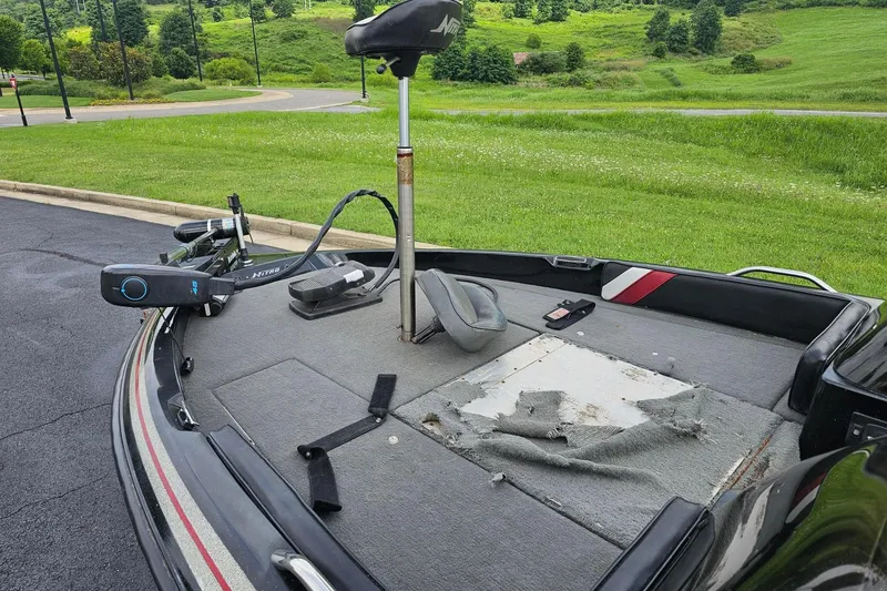 Slide: The Image of 1994 Nitro 180 FS boat with worn carpet and trolling motor, parked on asphalt near green landscape. - 8