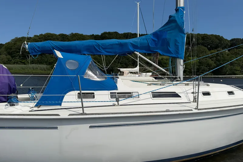Slide: The Image of 1986 Pearson 33 sailboat with blue sail cover docked by lush green shoreline. - 22