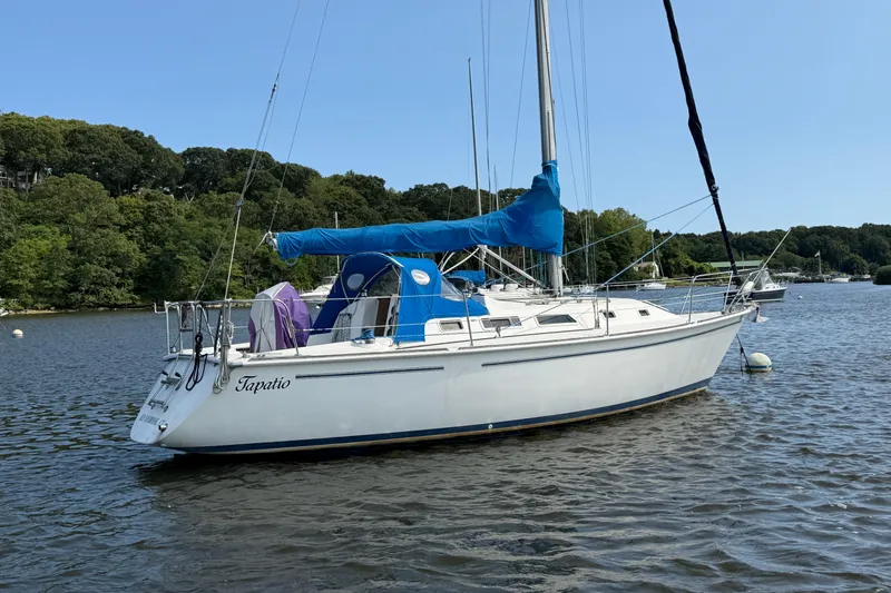 The Image of 1986 Pearson 33 sailboat anchored on a calm lake with lush green shoreline. - 0