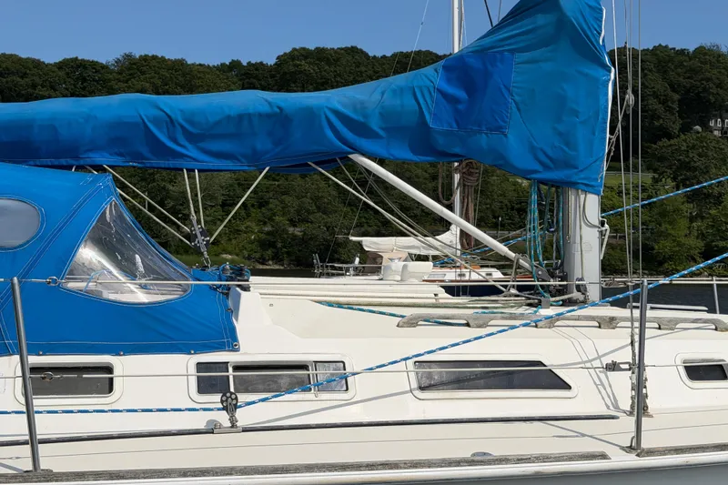Slide: The Image of 1986 Pearson 33 sailboat with blue canvas cover, docked near lush greenery. - 21