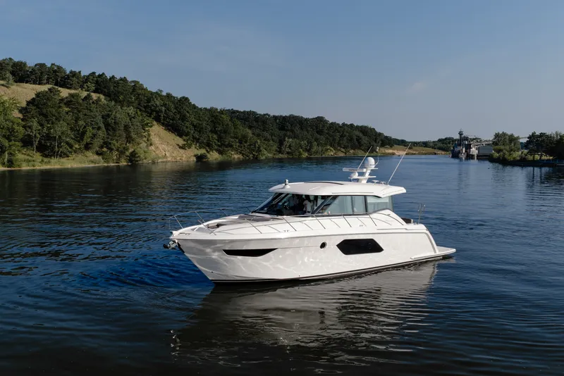 The Image of 2020 Tiara Yachts C49 Coupe cruising on a serene river with lush green banks. - 1
