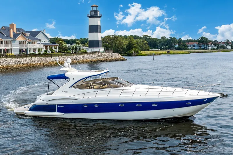 The Image of 2003 Cruisers 5470 Express yacht cruising near a lighthouse and waterfront homes. - 1