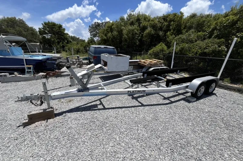 Slide: The Image of Boat trailer on gravel lot, surrounded by trees and boats, under a clear blue sky. - 8