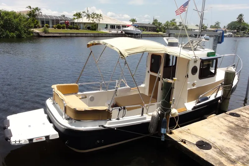The Image of 2012 Ranger Tugs R-21 EC docked, featuring a beige canopy and American flag. - 0