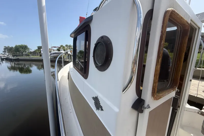 Slide: The Image of 2012 Ranger Tugs R-21 EC boat docked by calm waters, showcasing cabin details. - 11