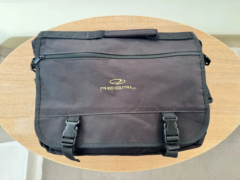 Slide: The Image of Black Regal bag with zipper and buckles on a wooden table. - 48