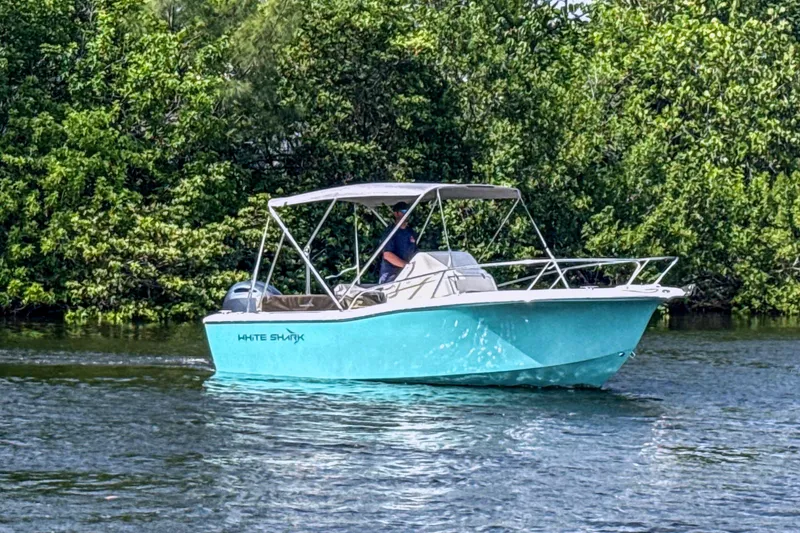 Slide: The Image of A turquoise 2023 White Shark 210CC boat on calm water, surrounded by lush greenery. - 11