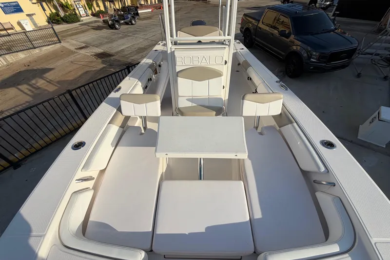 Slide: The Image of 2018 Robalo 246 Cayman boat interior with seating and table, parked near a truck. - 19