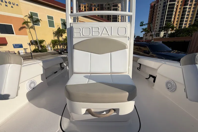 Slide: The Image of 2018 Robalo 246 Cayman boat interior with cushioned seating and marina backdrop. - 20