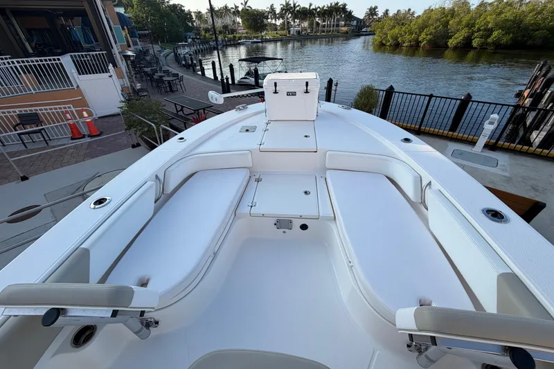 Slide: The Image of 2018 Robalo 246 Cayman boat interior with white seating, docked by a scenic waterfront. - 12