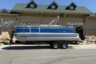 The Image of 2026 Sun Tracker Fishin' Barge 20 DLX pontoon boat on trailer, parked outside dealership. - 0