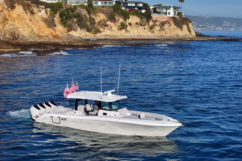 Slide: The Image of A 2026 HCB 42 Lujo cruising along a rocky coastline with multiple flags at the stern. - 8