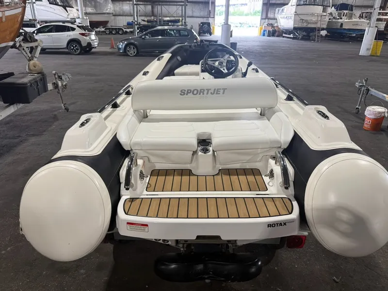 Slide: The Image of A 2019 Williams Jet Tender 395 Sport Jet in a warehouse, featuring a wooden deck and helm. - 1
