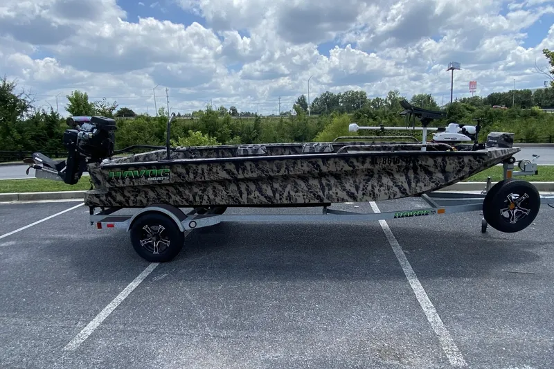 The Image of 2022 Havoc 1860 DBST camo boat on trailer, parked in a lot under cloudy sky. - 1