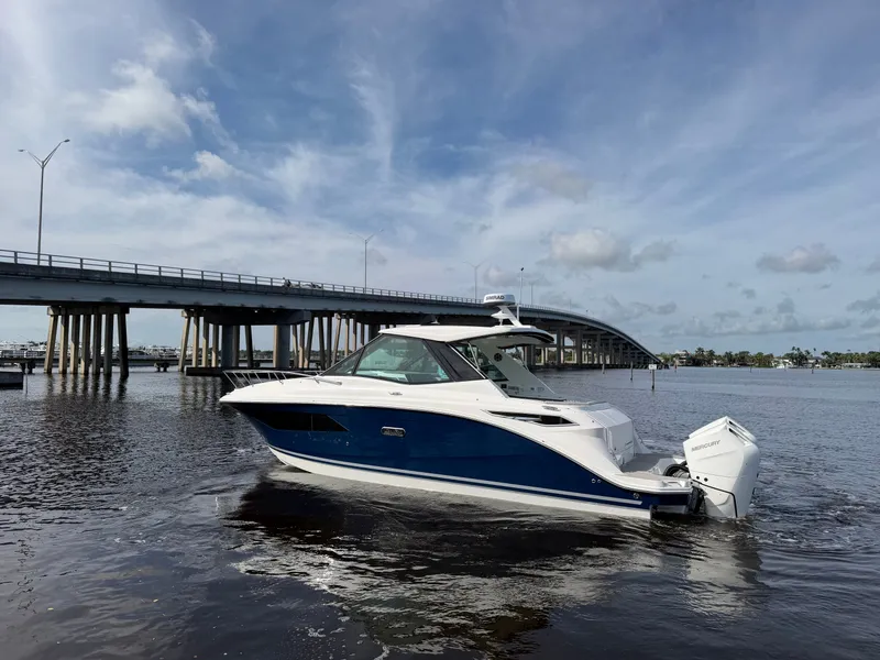 Slide: The Image of A 2027 Sea Ray Sundancer 320 Outboard on calm water near a bridge. - 16