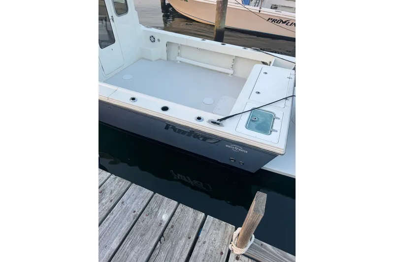 Slide: The Image of 2023 Parker 2320 SL Sport Cabin boat docked, showcasing spacious deck and fishing rod holder. - 2