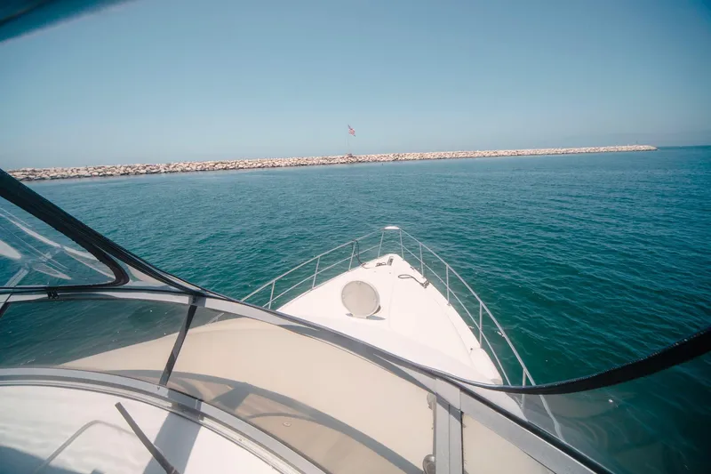 Slide: The Image of 1996 CRUISERS YACHTS 3580 Flybridge navigating calm blue waters near a rocky shoreline. - 32