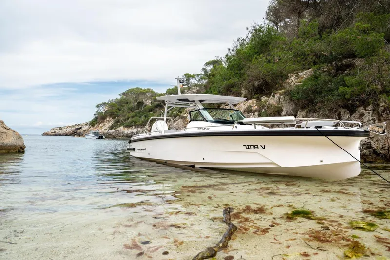 Slide: The Image of 2027 Axopar 29 Sun-Top boat anchored in a scenic, rocky coastal area. - 3