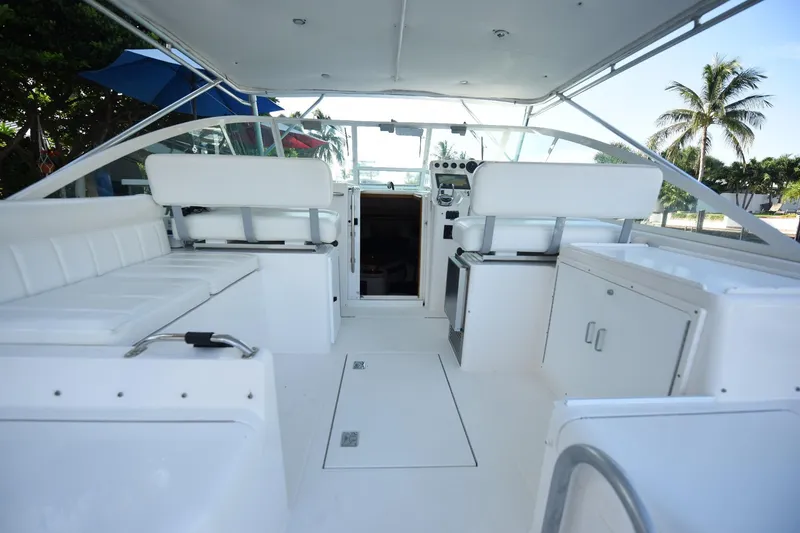 Slide: The Image of 2002 Cabo 35 Express boat interior with white seating and helm, tropical backdrop. - 46