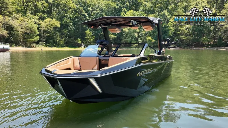 Slide: The Image of A sleek black Nautique G23 boat from 2027 floats on a calm lake, surrounded by trees. - 6