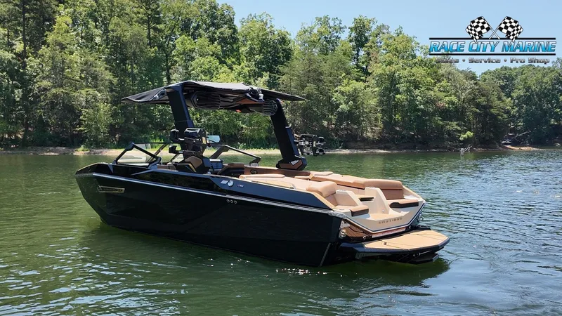 Slide: The Image of A sleek, black Nautique G23 boat from 2027 floats on a calm lake, surrounded by trees. - 7