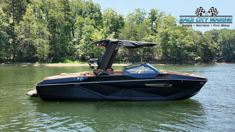 The Image of A sleek, black Nautique G23 boat from 2027 floats on a calm lake, surrounded by trees. - 1