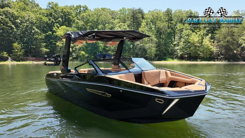 Slide: The Image of A sleek, black Nautique G23 boat from 2027 floats on a calm lake, surrounded by trees. - 5