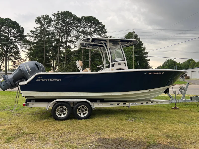 Slide: The Image of 2018 Sportsman Open 252 Center Console on a trailer, with dual outboard engines, parked in front of trees. - 1