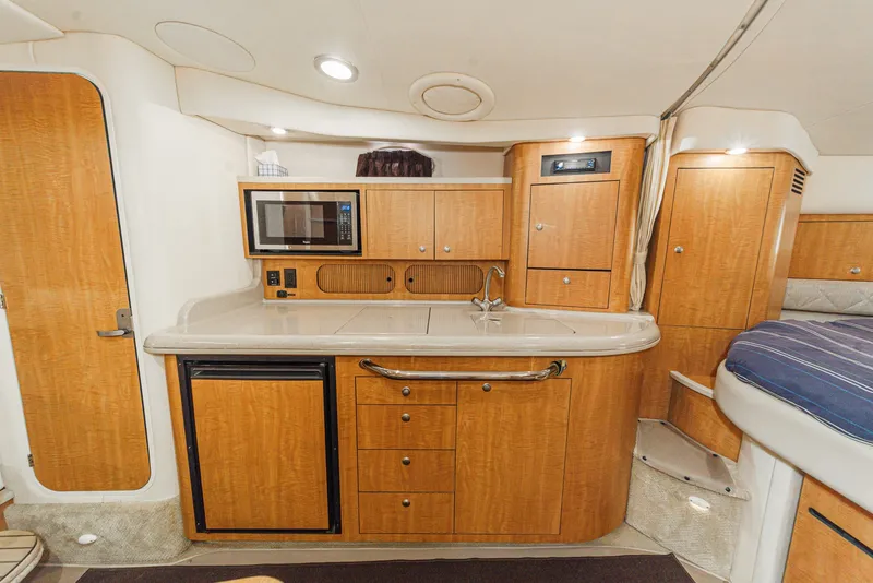 Slide: The Image of The interior of a 2006 Sea Ray 340 Sundancer features a well-equipped galley with wooden cabinetry. - 26